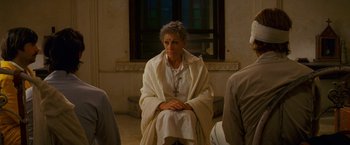 Movie still from “The Darjeeling Limited” (2007), directed by Wes Anderson – An older woman sitting on the floor with her hands folded on her knees; Medium shot, Over the shoulder angle