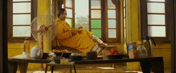 Movie still from “The Darjeeling Limited” (2007), directed by Wes Anderson – A man sitting on a chair in a room with bowls of food; Wide shot, Low angle