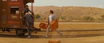 Movie still from “The Darjeeling Limited” (2007), directed by Wes Anderson – A man walking down a train track with two suitcases; Wide shot, Low angle