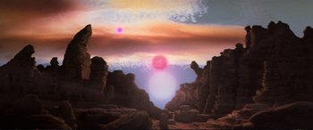 Movie still from “The Dark Crystal” (1982), directed by Frank Oz – The sun is setting in the sky over a rocky area; Extreme Wide shot, Low angle