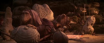 Movie still from “The Dark Crystal” (1982), directed by Frank Oz – A man that is sitting on the ground next to a rock; Wide shot, High angle
