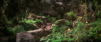 Movie still from “The Dark Crystal” (1982), directed by Frank Oz – Two people sitting on rocks in a lush green forest; Extreme Wide shot, High angle