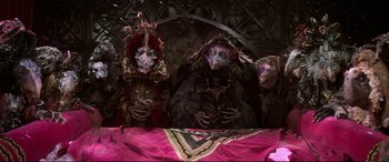 Movie still from “The Dark Crystal” (1982), directed by Frank Oz – A group of people dressed in costumes sitting next to a table; Wide shot, High angle