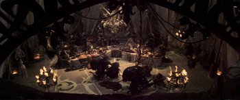 Movie still from “The Dark Crystal” (1982), directed by Frank Oz – A group of people sitting around a table with food on top of it; Wide shot, High angle