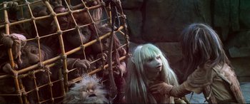 Movie still from “The Dark Crystal” (1982), directed by Frank Oz – A woman with long white hair standing in front of a cage; Medium shot, High angle