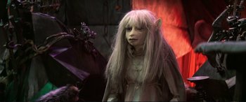 Movie still from “The Dark Crystal” (1982), directed by Frank Oz – A woman dressed up as a troll in front of a fire background; Close Up shot, High angle
