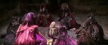 Movie still from “The Dark Crystal” (1982), directed by Frank Oz – A group of people dressed in purple and white costumes; Wide shot, High angle