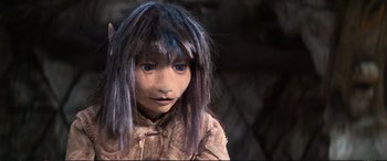 Movie still from “The Dark Crystal” (1982), directed by Frank Oz – A young girl with purple hair and blue eyes looking at the camera; Close Up shot, High angle