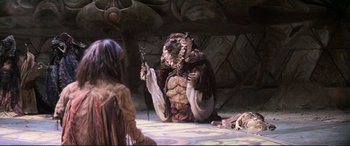 Movie still from “The Dark Crystal” (1982), directed by Frank Oz – A man dressed as an animal holding a staff in his hand; Wide shot, Over the shoulder angle