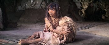 Movie still from “The Dark Crystal” (1982), directed by Frank Oz – A young girl dressed as a elf holding a stuffed animal; Medium shot, High angle