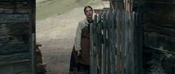 Movie still from “The Dark Valley” (2014), directed by Andreas Prochaska – A woman standing in front of a wooden fence; Medium shot, Over the shoulder angle