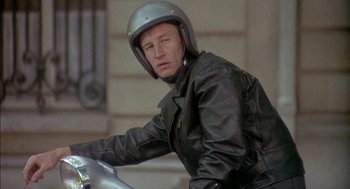 Movie still from “The Day of the Jackal” (1973), directed by Fred Zinnemann – A man wearing a leather jacket and helmet on a motorcycle; Close Up shot, Low angle
