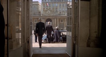 Movie still from “The Day of the Jackal” (1973), directed by Fred Zinnemann – A group of people standing on the sidewalk; Wide shot, Over the shoulder angle