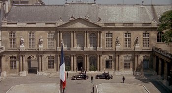 Movie still from “The Day of the Jackal” (1973), directed by Fred Zinnemann – A large building with cars parked in front of it; Extreme Wide shot, High angle