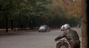 Movie still from “The Day of the Jackal” (1973), directed by Fred Zinnemann – Two people on a motorcycle and a car on the road; Wide shot, High angle