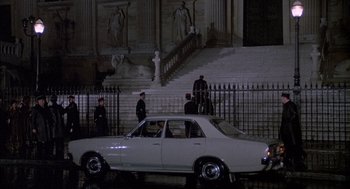 Movie still from “The Day of the Jackal” (1973), directed by Fred Zinnemann – A white car parked in front of a building; Extreme Wide shot, High angle