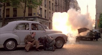 Movie still from “The Day of the Jackal” (1973), directed by Fred Zinnemann – A man sitting on the ground next to an old car; Wide shot, High angle