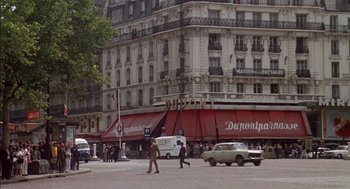 Movie still from “The Day of the Jackal” (1973), directed by Fred Zinnemann – People walking on the street in front of a large building; Extreme Wide shot, High angle