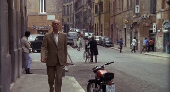 Movie still from “The Day of the Jackal” (1973), directed by Fred Zinnemann – A man in a brown suit walking down the street; Wide shot, Low angle