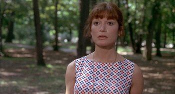 Movie still from “The Day of the Jackal” (1973), directed by Fred Zinnemann – A woman in a red , white , and blue dress in a park; Close Up shot, Over the shoulder angle