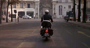Movie still from “The Day of the Jackal” (1973), directed by Fred Zinnemann – A person riding a motorcycle down a street; Wide shot, Low angle
