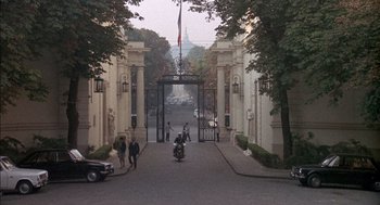 Movie still from “The Day of the Jackal” (1973), directed by Fred Zinnemann – A man riding a motorcycle down a street next to a building; Extreme Wide shot, High angle