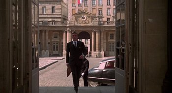 Movie still from “The Day of the Jackal” (1973), directed by Fred Zinnemann – A man in a suit and tie walking down a street; Wide shot, Low angle