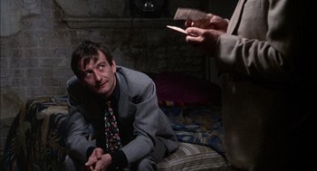 Movie still from “The Day of the Jackal” (1973), directed by Fred Zinnemann – A man sitting on the ground with a knife in his hand; Medium shot, Over the shoulder angle