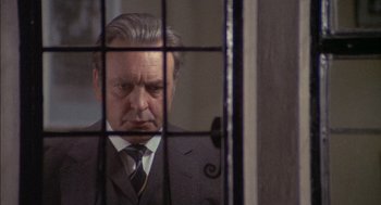 Movie still from “The Day of the Jackal” (1973), directed by Fred Zinnemann – A man in a suit and tie behind bars looking out a window; Close Up shot, Over the shoulder angle