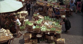 Movie still from “The Day of the Jackal” (1973), directed by Fred Zinnemann – A group of people standing next to a pile of fruit; Wide shot, Overhead angle
