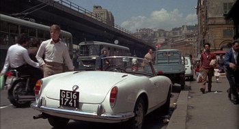 Movie still from “The Day of the Jackal” (1973), directed by Fred Zinnemann – An old car is parked on the side of the road; Wide shot, Over the shoulder angle