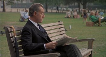 Movie still from “The Day of the Jackal” (1973), directed by Fred Zinnemann – A man sitting on top of a wooden park bench; Medium shot, Low angle