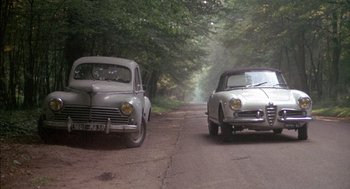 Movie still from “The Day of the Jackal” (1973), directed by Fred Zinnemann – Two vintage cars are driving down the road; Wide shot, High angle