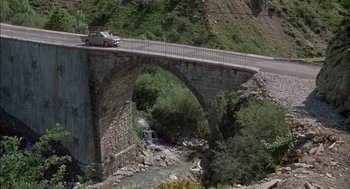 Movie still from “The Day of the Jackal” (1973), directed by Fred Zinnemann – A car is driving on a bridge over a river; Extreme Wide shot, High angle