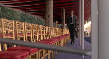Movie still from “The Day of the Jackal” (1973), directed by Fred Zinnemann – A man in a suit walking in front of rows of chairs; Wide shot, High angle