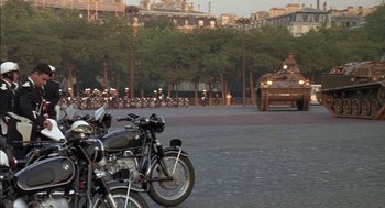Movie still from “The Day of the Jackal” (1973), directed by Fred Zinnemann – Two motorcycles are parked in front of an armored vehicle; Wide shot, High angle