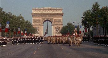 Movie still from “The Day of the Jackal” (1973), directed by Fred Zinnemann – A group of people marching down a street in front of an arch; Extreme Wide shot, Low angle