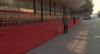 Movie still from “The Day of the Jackal” (1973), directed by Fred Zinnemann – Two people walking down a sidewalk near a red carpet; Extreme Wide shot, High angle