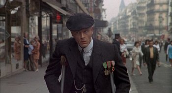 Movie still from “The Day of the Jackal” (1973), directed by Fred Zinnemann – A man in a black suit and a hat is walking down the street; Medium shot, Low angle