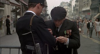 Movie still from “The Day of the Jackal” (1973), directed by Fred Zinnemann – Two men in suits and hats are looking at a cell phone; Medium shot, Over the shoulder angle