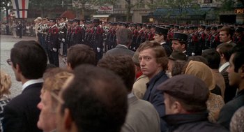 Movie still from “The Day of the Jackal” (1973), directed by Fred Zinnemann – A crowd of people standing in front of a line of men in uniform; Wide shot, Over the shoulder angle