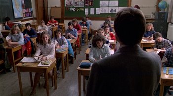Movie still from “The Dead Zone” (1983), directed by David Cronenberg – A group of people sitting at desks in a classroom; Wide shot, Over the shoulder angle