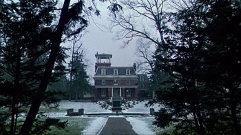 Movie still from “The Dead Zone” (1983), directed by David Cronenberg – A red brick house surrounded by trees in the snow; Extreme Wide shot, Low angle