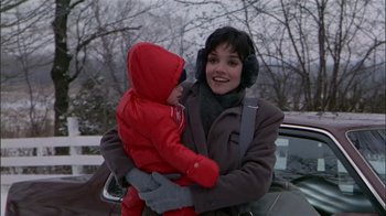 Movie still from “The Dead Zone” (1983), directed by David Cronenberg – A woman holding a baby in her arms next to a car; Medium shot, Over the shoulder angle