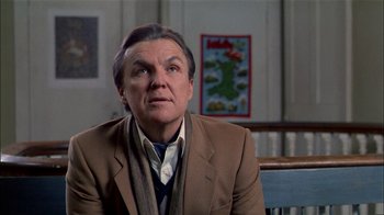 Movie still from “The Dead Zone” (1983), directed by David Cronenberg – A man wearing a suit and tie sitting in front of a painting; Close Up shot, Low angle