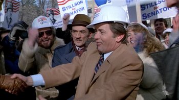 Movie still from “The Dead Zone” (1983), directed by David Cronenberg – A group of people wearing hard hats in a crowd of people; Medium shot, Low angle