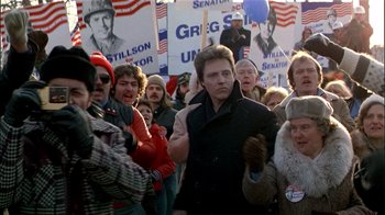 Movie still from “The Dead Zone” (1983), directed by David Cronenberg – A group of people walking down a street with political signs; Medium shot, High angle