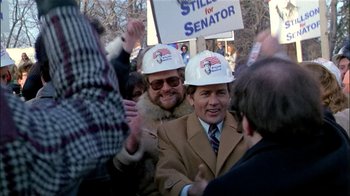 Movie still from “The Dead Zone” (1983), directed by David Cronenberg – A group of people wearing hard hats at a political rally; Medium shot, Over the shoulder angle