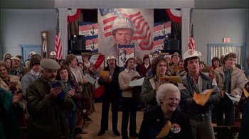 Movie still from “The Dead Zone” (1983), directed by David Cronenberg – A group of people standing in front of an american flag; Medium shot, High angle