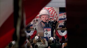 Movie still from “The Dead Zone” (1983), directed by David Cronenberg – A crowd of people standing in front of a painting of a man; Wide shot, High angle